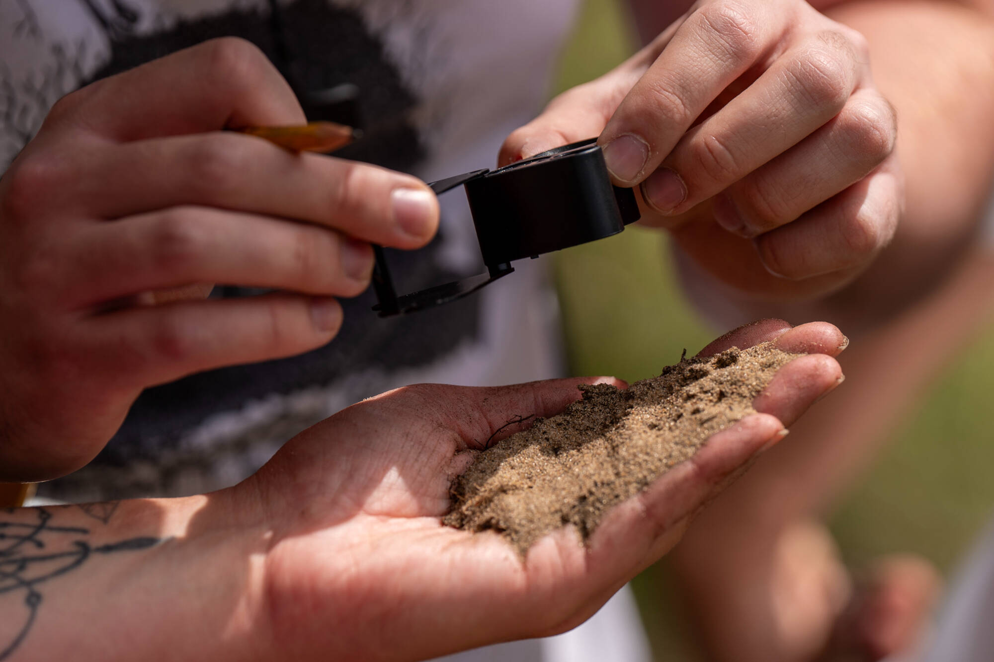 student holding sand and examining it through a magnifying loop